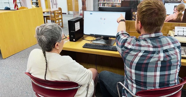 Jacob teaches a patron how to use a computer.