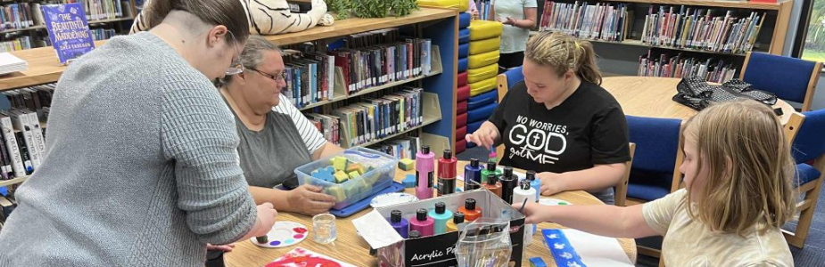Two teen girls and two adult women are creating splatter and sponge painting at a circular table.
