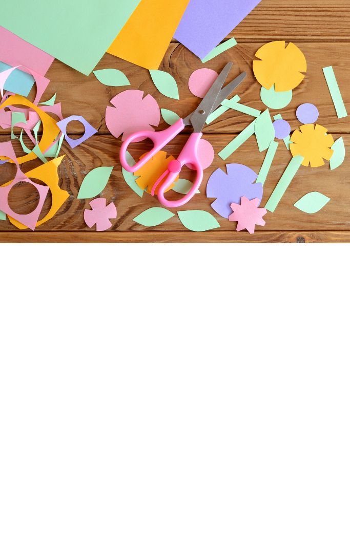 Pink scissors and colorful paper on a wooden table.